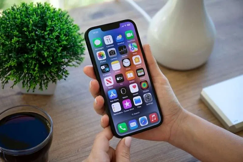Woman hand holding iPhone 14 with home screen IOS 16